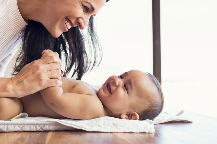 Happy mum playing with baby while changing his nappy