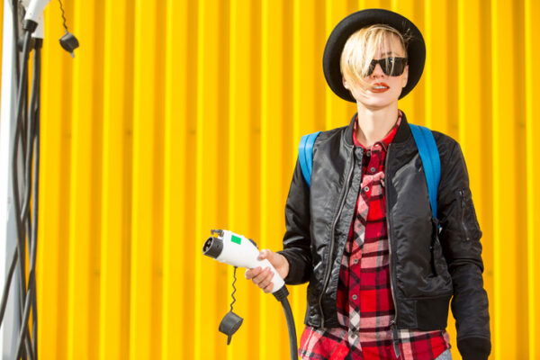 Happy woman standing by electric car, holding charger