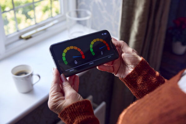 Senior woman holding smart meter by radiator during cost of living crisis