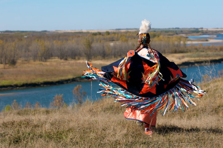 A woman performing a First Nations fancy shawl dance in a field alongside the river in Saskatoon, Saskatchewan