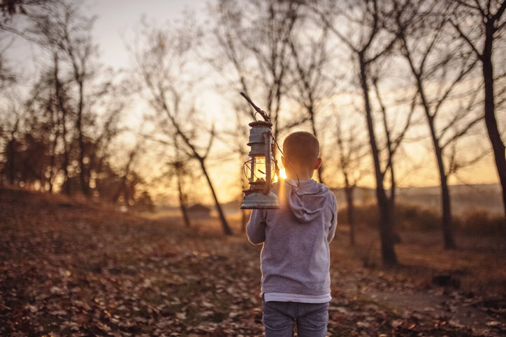 Boy standing in the woods and holding old lamp on a stick