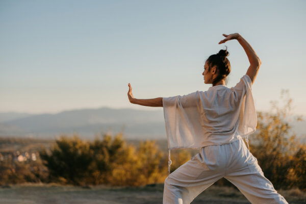 Woman doing tai chi in a meadow at sunset