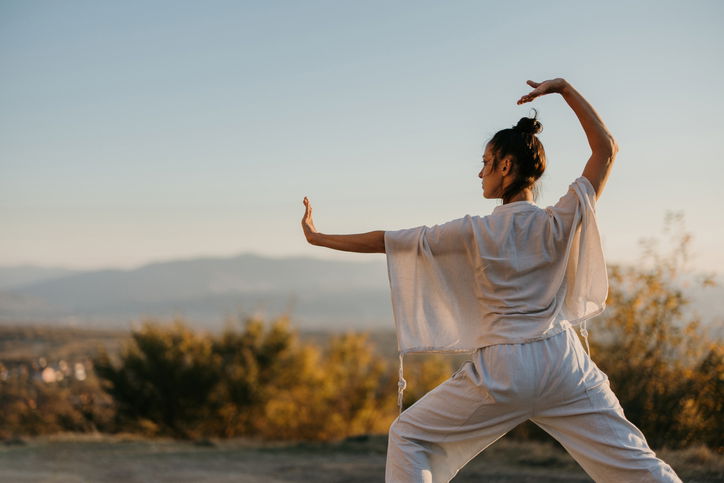 Woman doing tai chi in a meadow at sunset