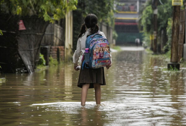 A girl returns from school wades across a flooded street after heavy rains, in Guwahati, India