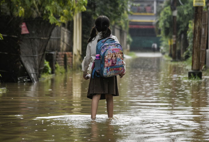 A girl returns from school wades across a flooded street after heavy rains, in Guwahati, India