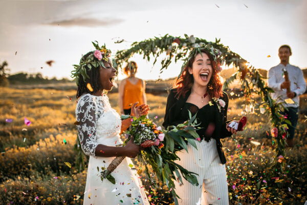 Two brides on wedding ceremony, surprised with confetti standing in a front of outdoor wedding arch