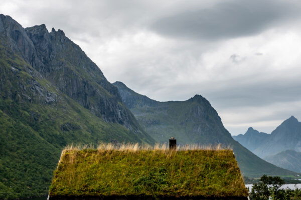Small house with a living roof next to a fjord with mountain range in background in the Lofoten Islands on a cloudy day of summer